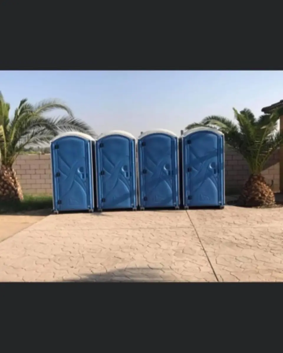 Four blue porta potties lined up on a paved lot